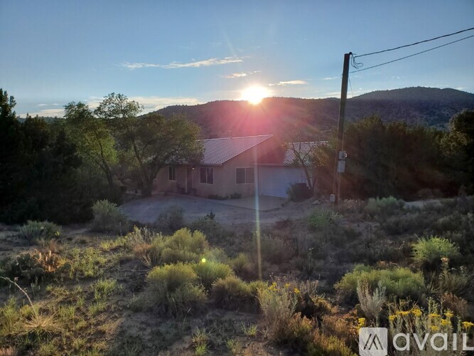 A house is situated in a field with the sun setting in the background.