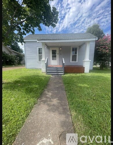 A small white house with a porch and a tree in front.