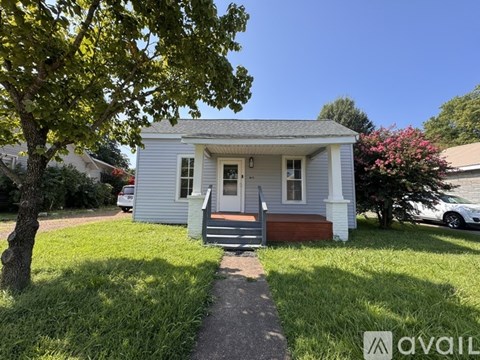 A small white house with a porch and a tree in front.