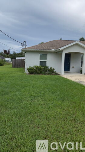 A house with a white exterior and a brown roof is shown with a grassy lawn in front.