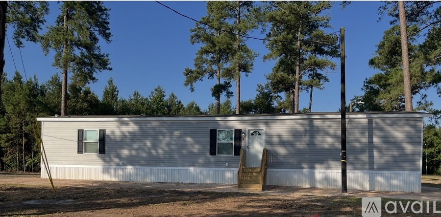 A house with a white exterior and a brown door is surrounded by trees.
