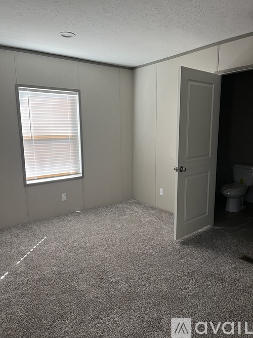 A room with a carpeted floor and a window with blinds.