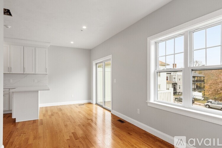 A spacious room with wooden floors and a large window overlooking a street.