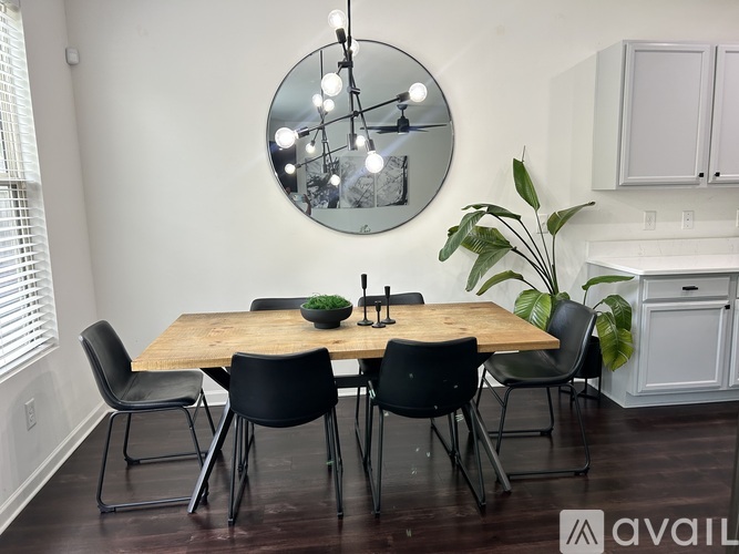 A dining room with a round mirror, a wooden table, and black chairs.