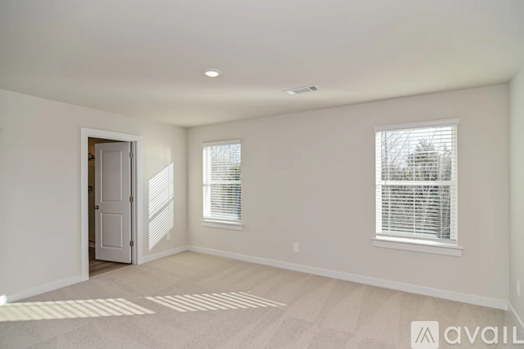 A room with a carpeted floor and two windows with blinds.