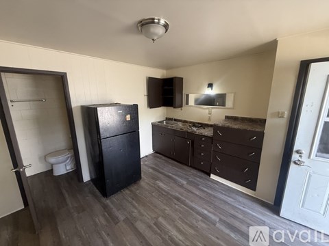 A kitchen with a black fridge, black cabinets, and a white toilet.