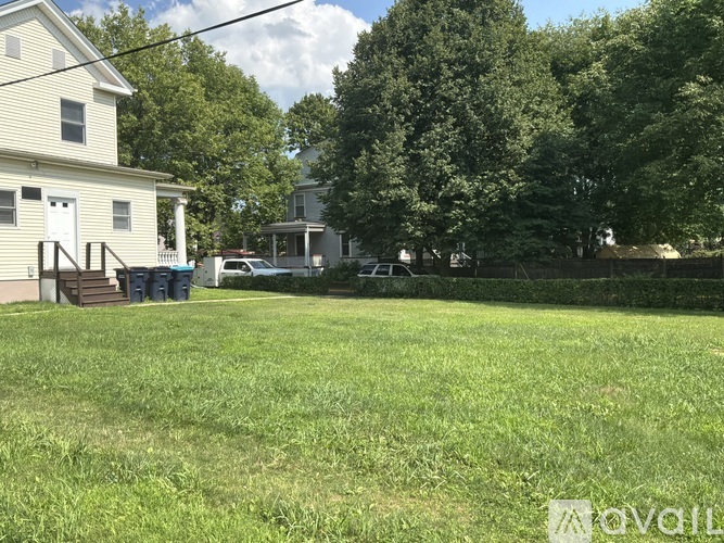 A grassy area in front of a house with a trash can and a fence.