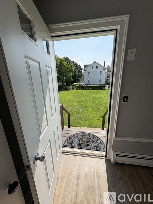 A white door opens to a backyard with a house in the distance.