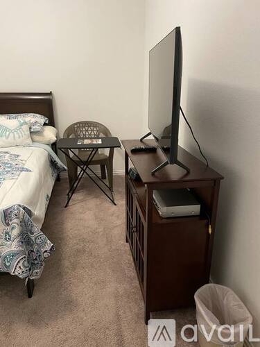 A bedroom with a bed, a chair, a table, and a television on a wooden stand.