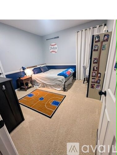 A bedroom with a bed, a fridge, and a basketball court rug on the floor.