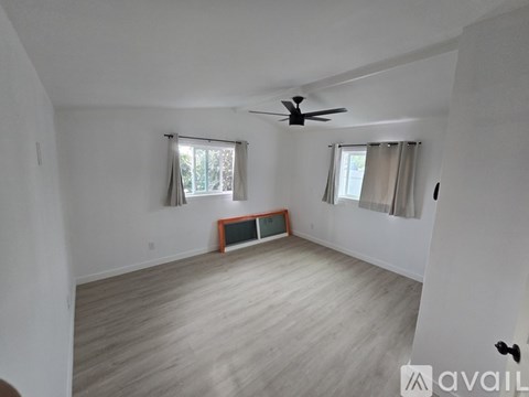 A room with a ceiling fan and two windows.