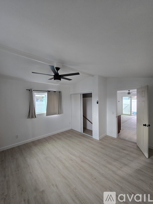 A spacious room with a ceiling fan and light wood flooring.