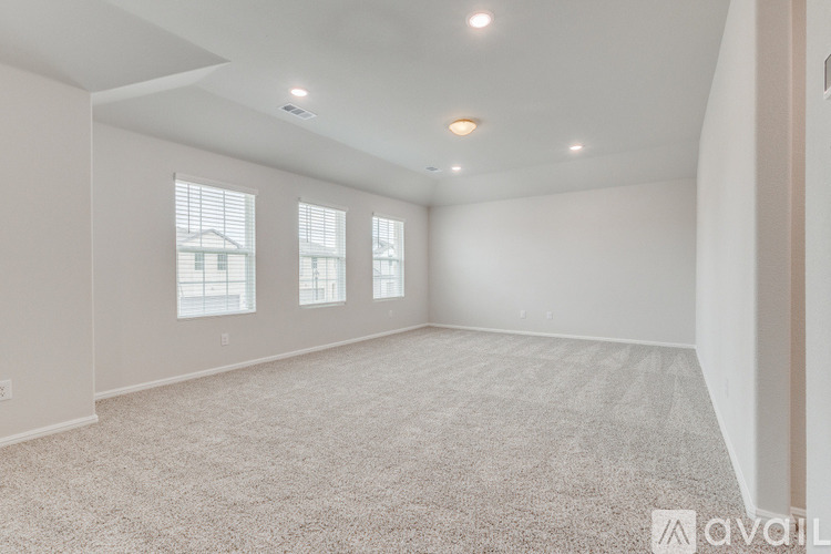 A spacious room with carpeted floor and three windows.