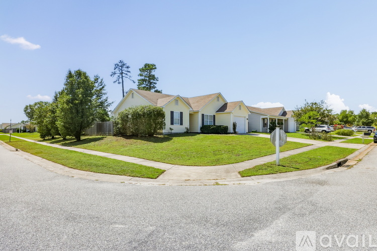A white house with a brown roof is surrounded by green grass and trees.
