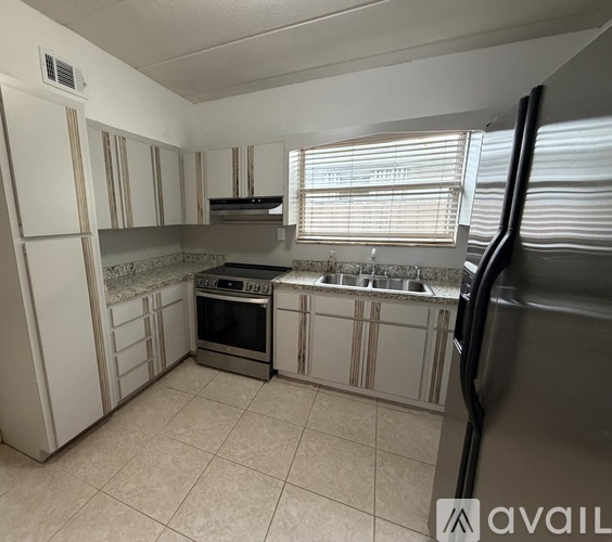 A kitchen with white cabinets and appliances, a window with blinds, and a tiled floor.
