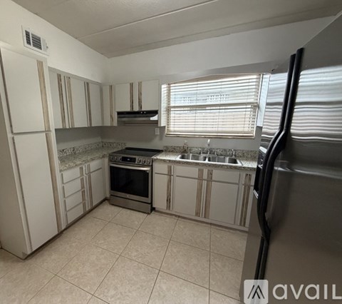 A kitchen with white cabinets and appliances, a window with blinds, and a tiled floor.