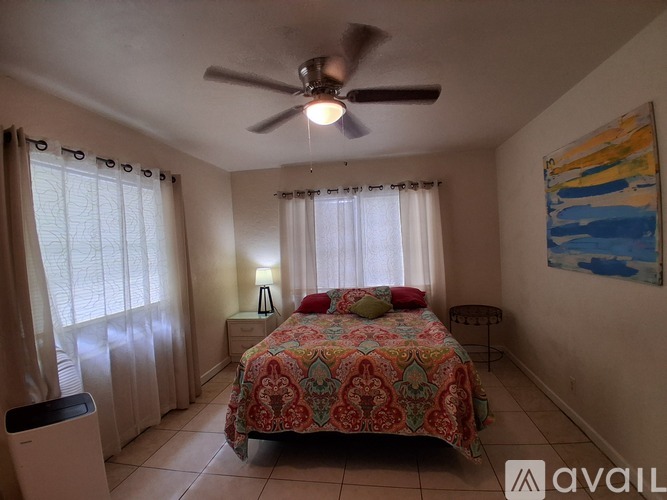 A bedroom with a bed, a ceiling fan, and a painting on the wall.