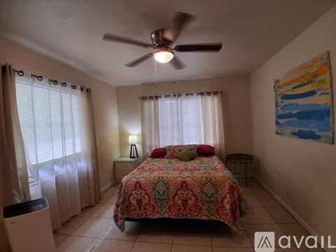 A bedroom with a bed, a ceiling fan, and a painting on the wall.