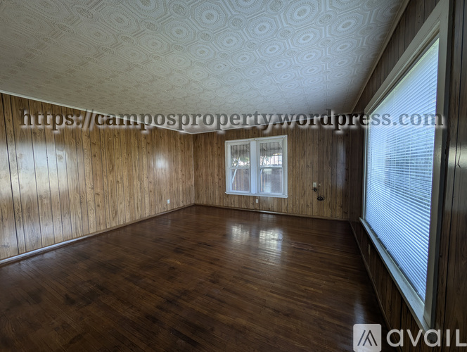 A room with wooden floors and walls, a window with blinds, and a ceiling with a patterned design.