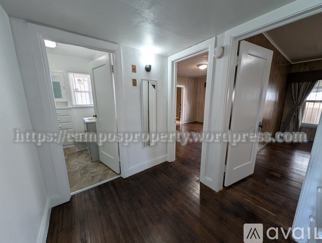 A spacious room with wooden floors and white walls, featuring a staircase and a large mirror.