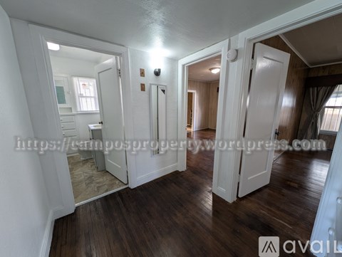 A spacious room with wooden floors and white walls, featuring a staircase and a large mirror.