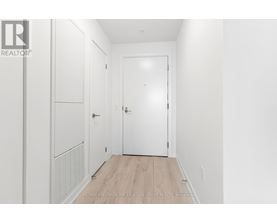 A white hallway with a door and a wall-mounted cabinet.