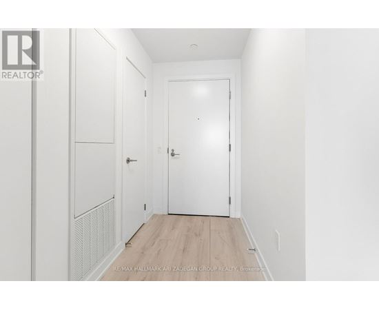 A white hallway with a door and a wall-mounted cabinet.