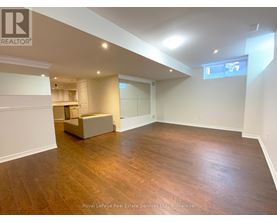 A spacious room with wooden flooring and white walls, featuring a built-in bench and a window.