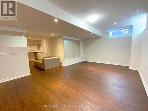 A spacious room with wooden flooring and white walls, featuring a built-in bench and a window.