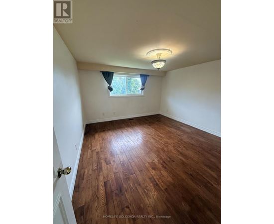 A room with wooden flooring and a window with a view of trees.