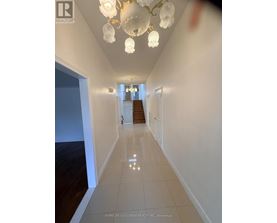 A hallway with a chandelier and a staircase in the background.