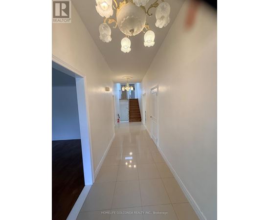 A hallway with a chandelier and a staircase in the background.