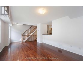 A spacious room with wooden floors and a staircase.