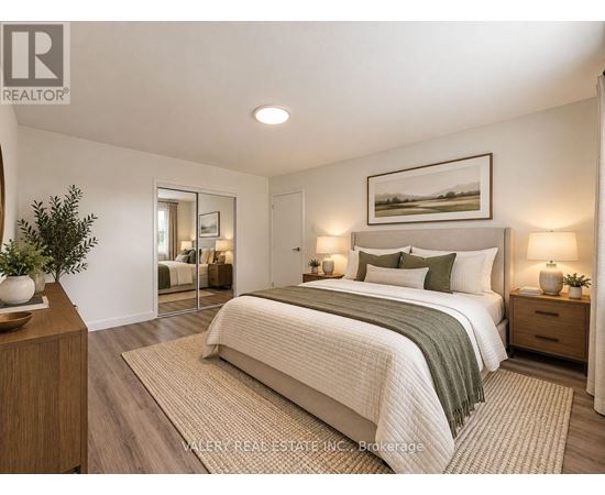 A bedroom with a large bed, a nightstand with a lamp, and a framed picture on the wall.