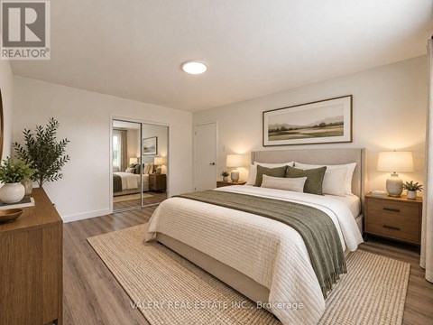 A bedroom with a large bed, a nightstand with a lamp, and a framed picture on the wall.