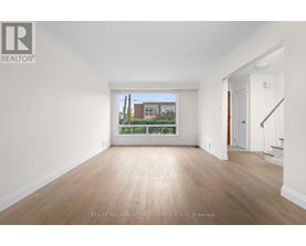 A spacious room with wooden floors and white walls, with a view of a building outside the window.