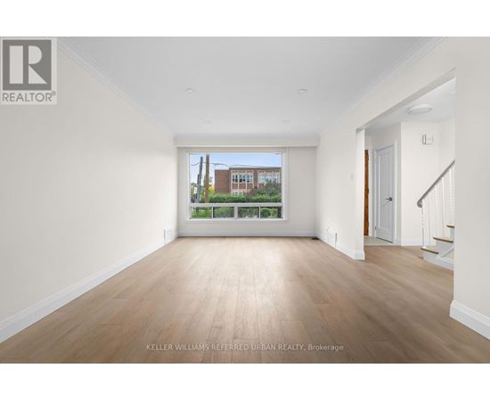 A spacious room with wooden floors and white walls, with a view of a building outside the window.