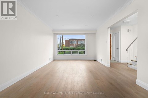 A spacious room with wooden floors and white walls, with a view of a building outside the window.