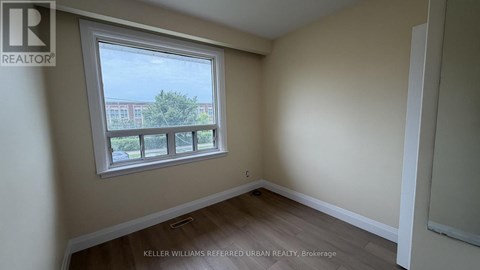 A room with a window showing a view of a building and trees outside.