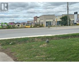 A grassy area in front of a road with a sign for REMAX WEST REALTY INC. Brokerage.