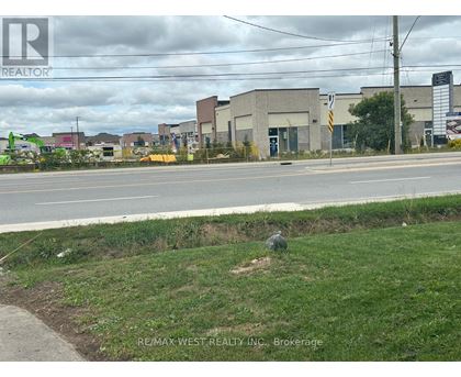 A grassy area in front of a road with a sign for REMAX WEST REALTY INC. Brokerage.