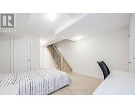 A bedroom with a bed, chair, and stairs in the background.