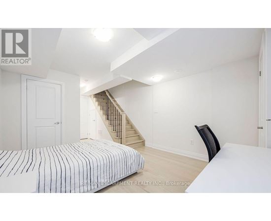 A bedroom with a bed, chair, and stairs in the background.