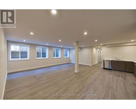 A spacious room with wooden flooring and a row of windows.