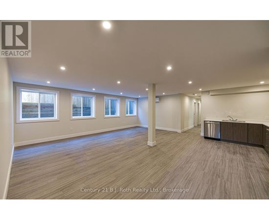 A spacious room with wooden flooring and a row of windows.