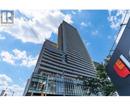 A tall building with a glass facade stands under a blue sky with clouds.