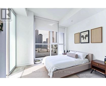 A bedroom with a large bed, a nightstand, and a window overlooking a cityscape.