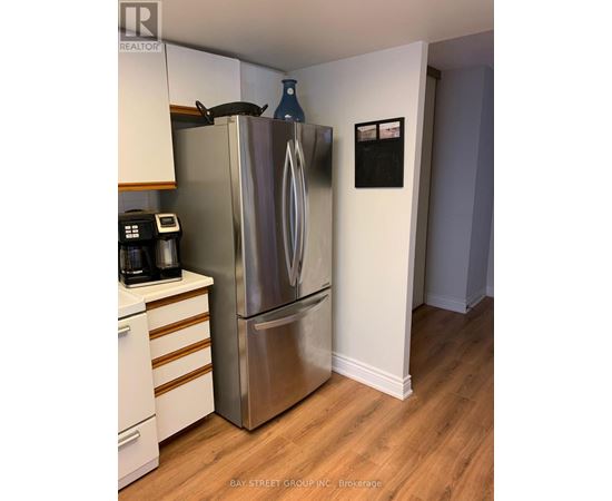A stainless steel refrigerator in a kitchen with wooden floors and white walls.