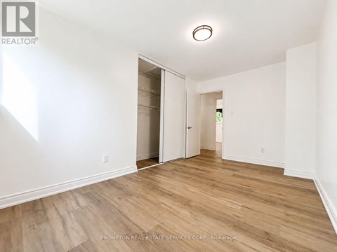 A room with wood flooring and white walls, with a doorway leading to another room.