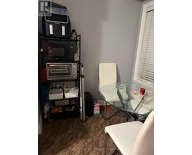 A room with a microwave on top of a shelf and a glass table with a white chair.